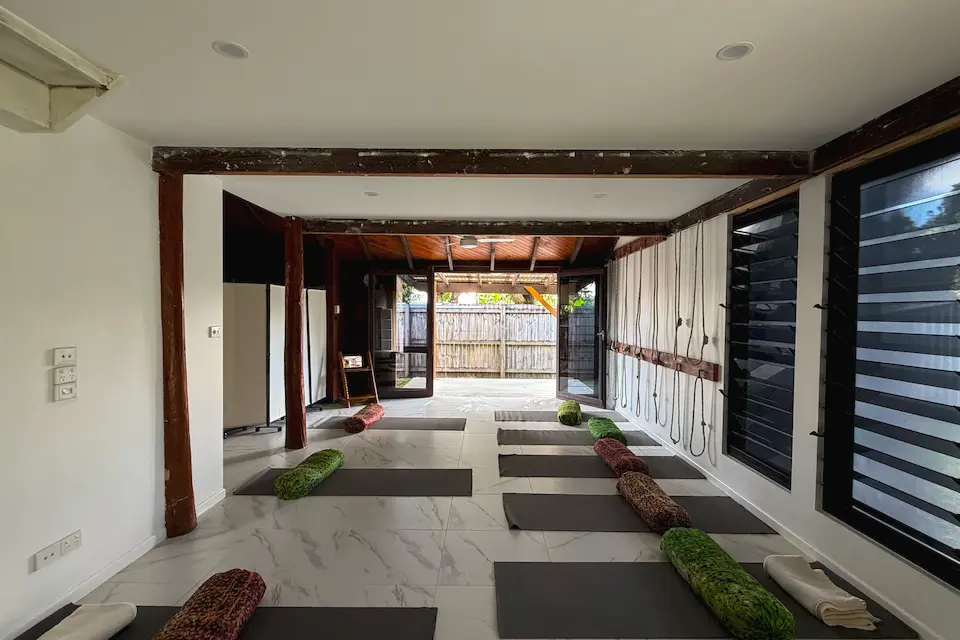 Inside the Kewarra Beach studio: timber beams and posts, mats and bolsters laid out on the marble floor, and glass doors opening onto the garden