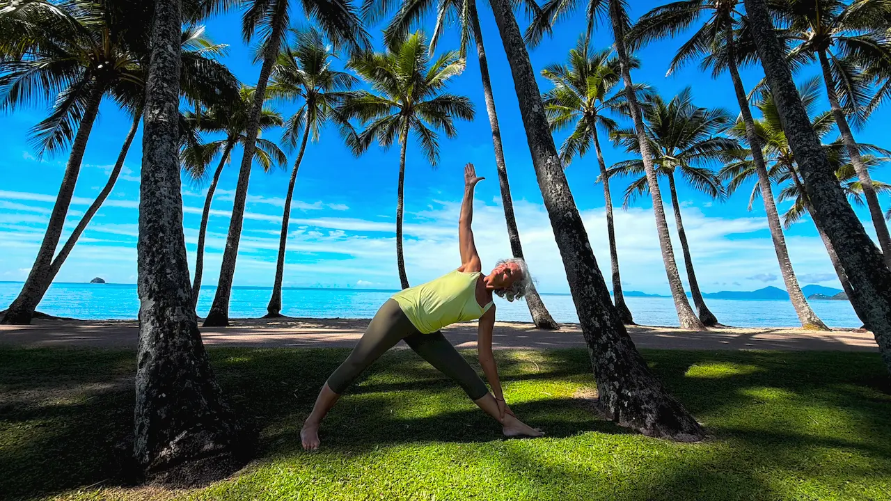 Susan Stackhouse in extended triangle pose, Utthita Trikonasana, in a grove of palms beside the sea at Kewarra Beach
