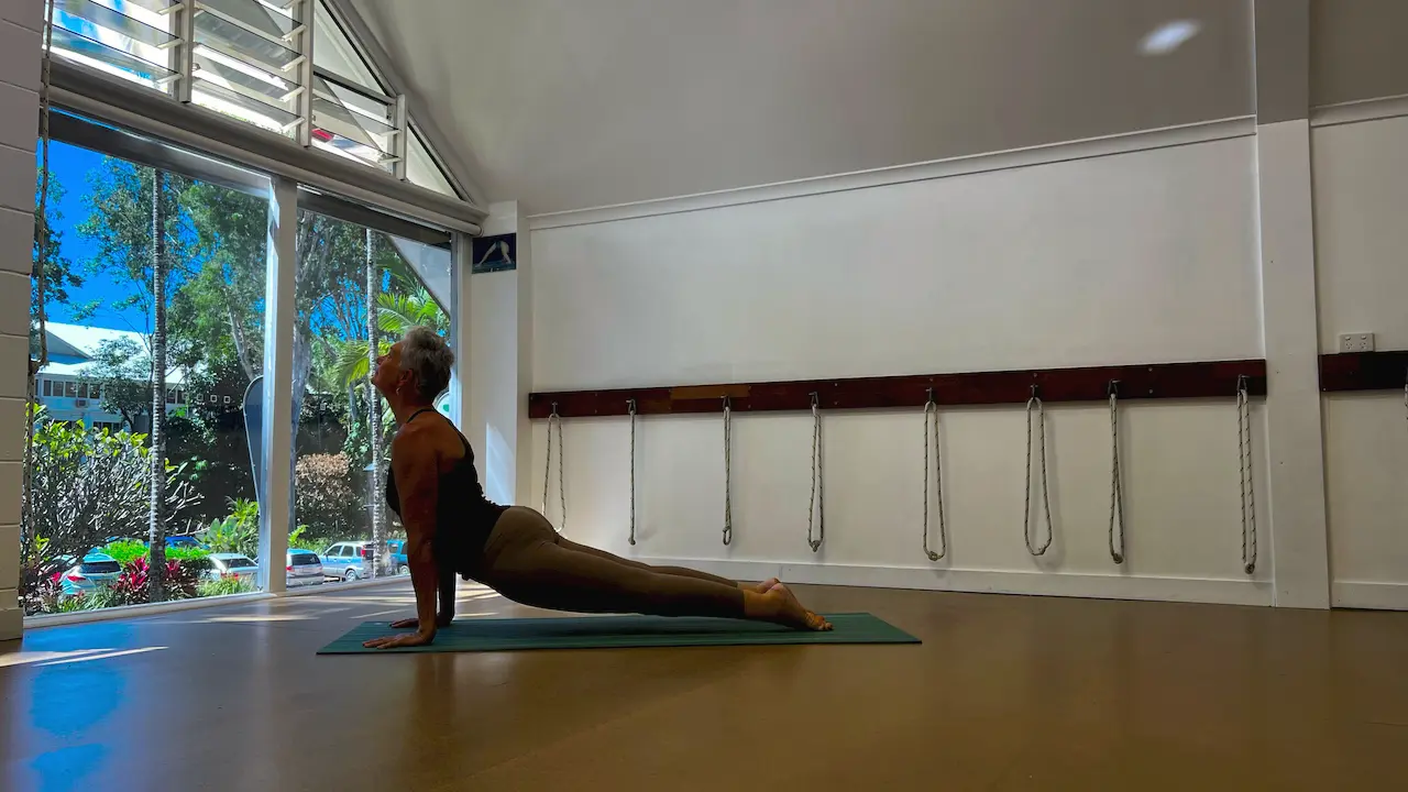 Susan Stackhouse in upward facing dog, Urdhva Mukha Svanasana, on a mat in the studio with the rope wall behind her