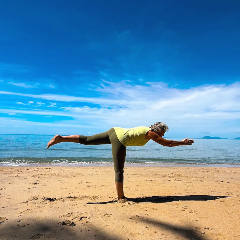 Susan Stackhouse balancing on one leg in Warrior III, Virabhadrasana III, on the sand at Kewarra Beach, her body level with the horizon
